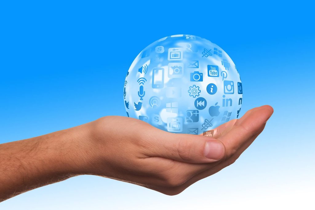 hand holds a transparent sphere displaying social networks and apps, on a blue background.